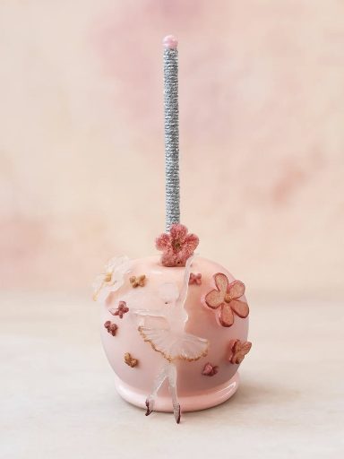 Zarte, rosa Zuckerapfel mit Blumen dekoriert und einem silbernen Stäbchen.